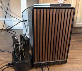 The server in its new smaller case, with its wire mesh sides and wooden front panel. Two hard disk drives are docked into a unit that's plugged in via USB. A white USB DVD drive sits on top.