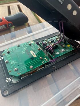 The back of the door button, with the back cover removed to reveal the electronics powering the button. There are large purple wires connecting the back cover to the board.