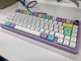 The MKC75 keyboard on a white desk. It has a pastel purple case, and white keys with pastel coloured accents: a purple CMD key, a blue alt key, and a green ISO enter key. The F-key row are all pastel coloured fruits.