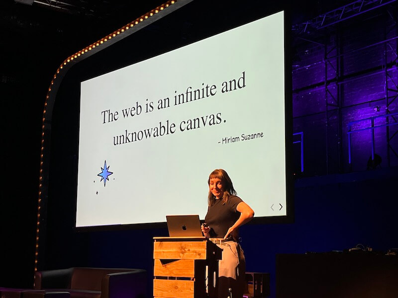 Cassie Evans stands in front of a slide that says 'The web is an infinite and unknowable canvas' - Miriam Suzanne