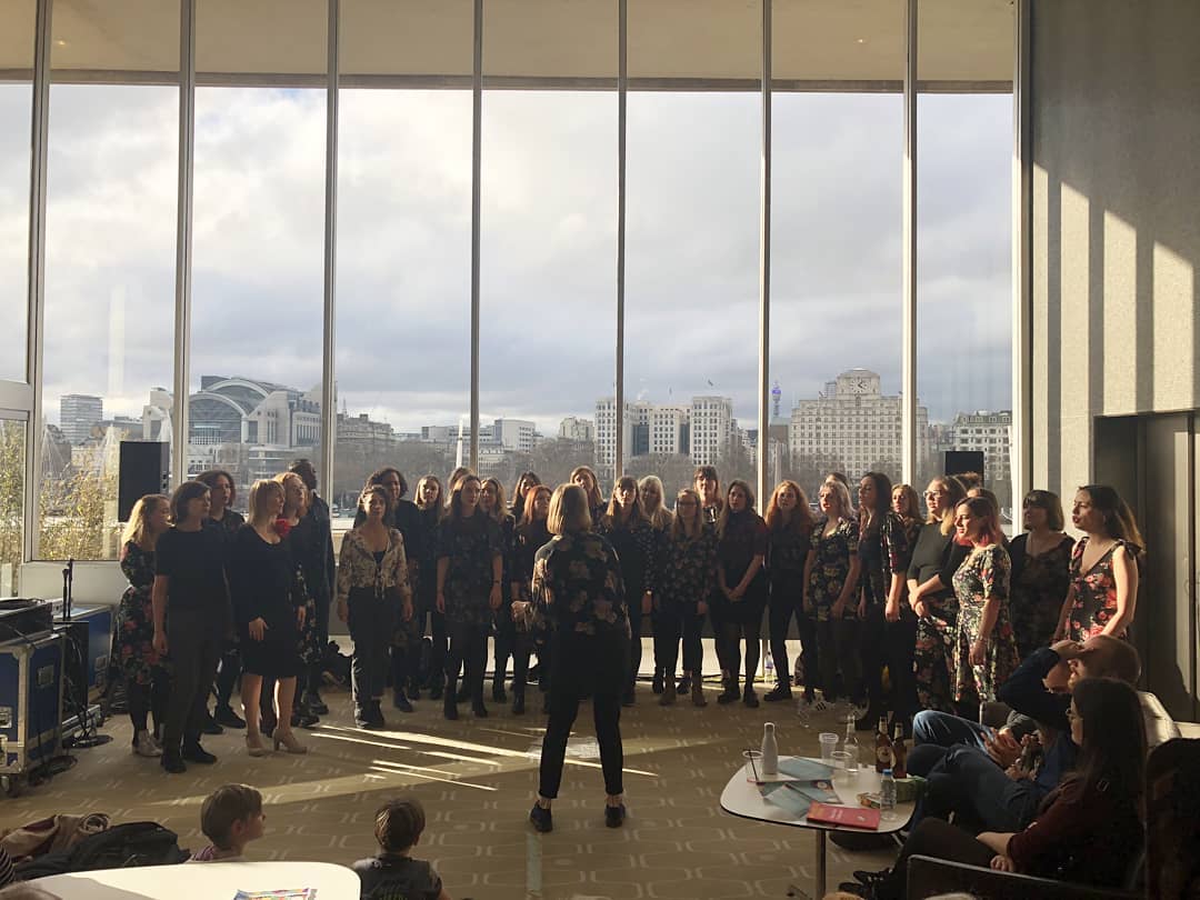The choir performing in the South Bank centre, wearing all black and floral. Behind then, through the windows, you can see the Thames and buildings along the north bank of the river
