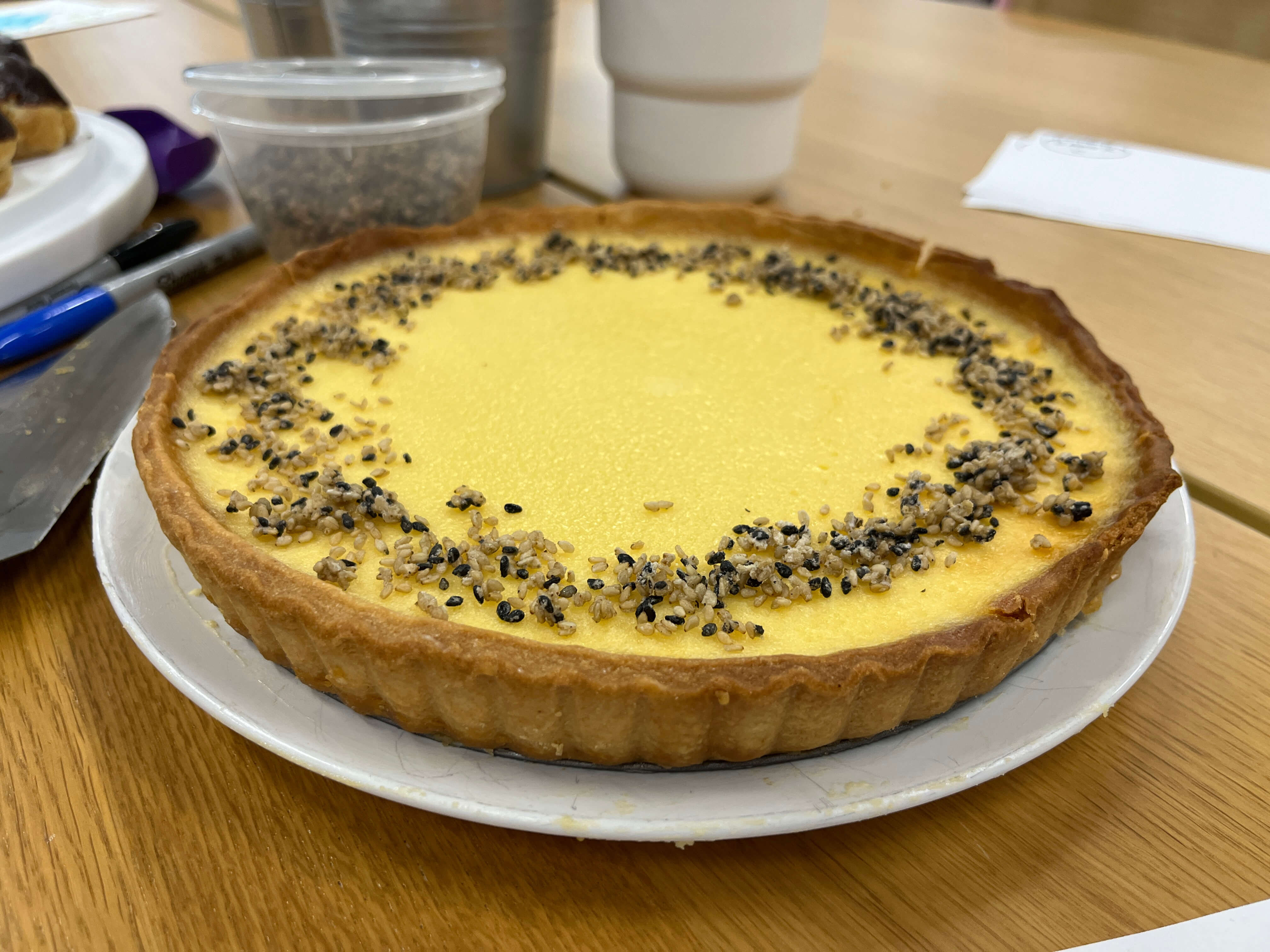 A pale yellow tart in a pastry case, with a sprinkling of black and white sesame seeds in a circle on top.