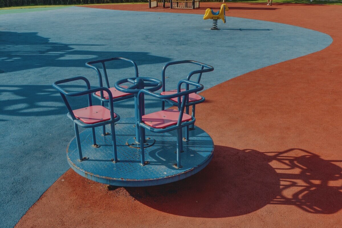 A faded blue merry-go-round with red seats in the middle of that spongy playground flooring