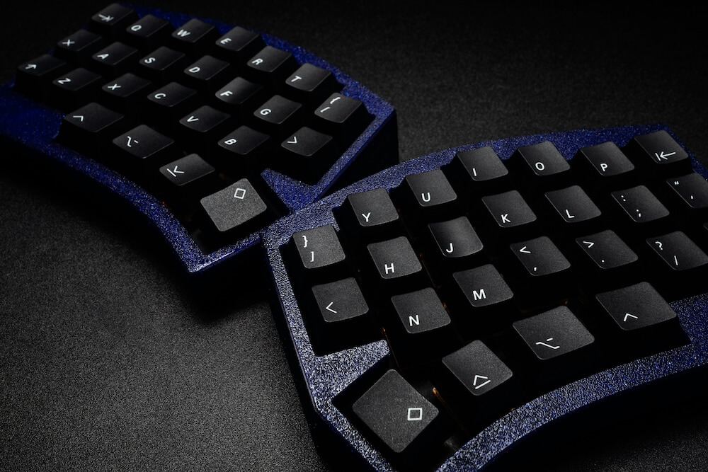 A dark blue split keyboard, one side in front of the other. It has black keycaps with white legends.