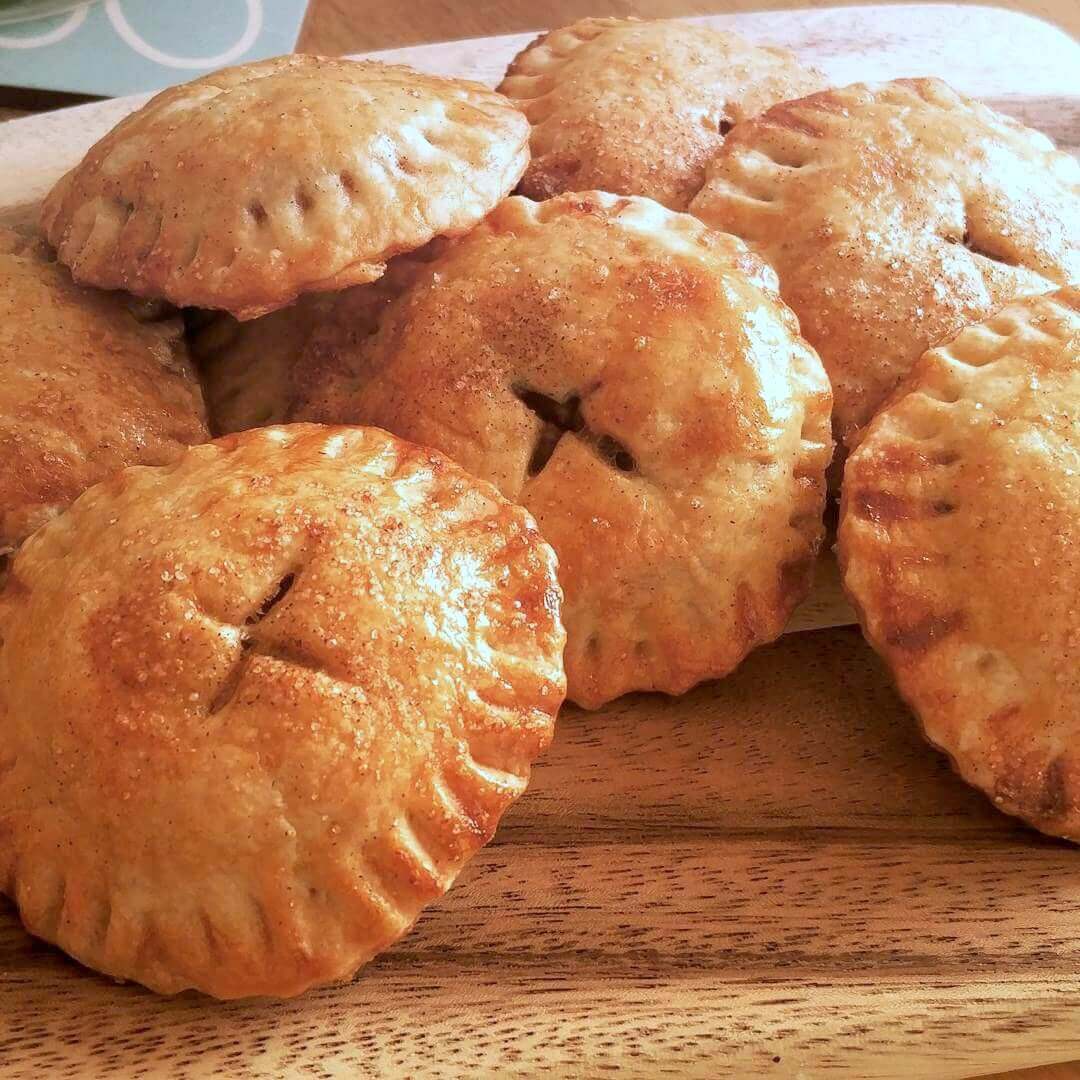 A close-up of golden apple pie-shaped cookies, glossy from an egg wash, sprinkled with sugar crystals.