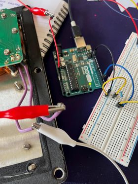 An Arduino microcontroller connected to the button with some crocodile clips via a prototyping breadboard. There's a resistor and various wires plugged into the breadboard.
