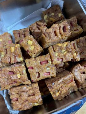 A tin of rhubarb and custard blondies, golden coloured squares studded with white chocolate and slices of rhubarb.