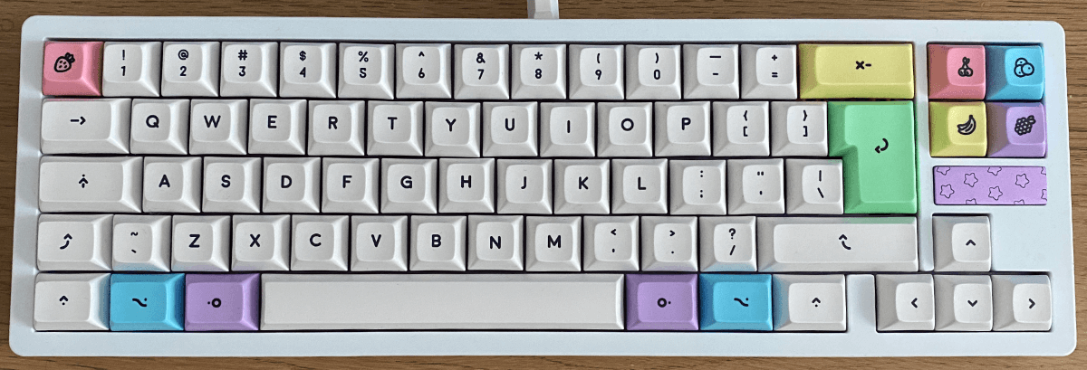 The ikki68 Aurora keyboard with white and pastel purple polycarbonate case. Most of the keys are off-white, the escape and pg up/pg down/home/end keys are pastel coloured with fruit legends. It is in Mac ISO layout with a split left shift.