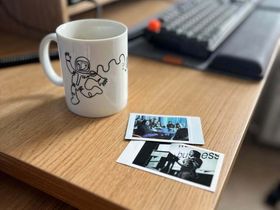 A mug with a line drawing of a spaceman on it, next to two Polaroid-style instant photos of me on stage at Beyond Tellerrand, and me at the breakfast table with two other speakers. 