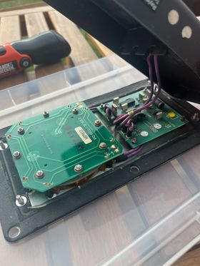 The back of the door button, with the back cover removed to reveal the electronics powering the button. There are large purple wires connecting the back cover to the board.