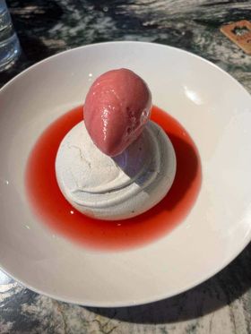 A scoop of rhubarb sorbet sits on top of a perfectly domed meringue, surrounded by a bright pink moat of rhubarb and jasmine sauce